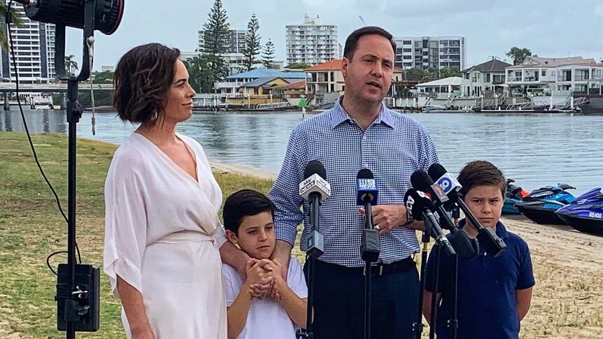Steve Ciobo  with his wife and two children with microphones and lights in front of them and water, boats and buildings behind