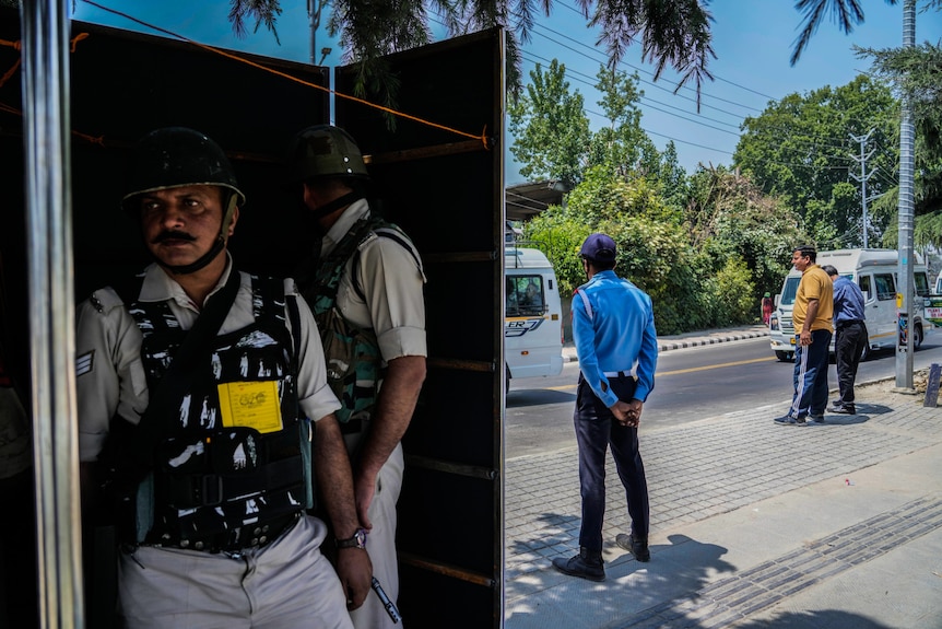 Two security guards hide behind a poster while others stand guard. 