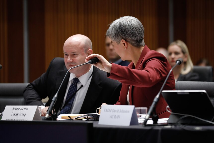 Penny Wong covers her microphone while speaking with Greg Moriarty at a Senate estimates hearing