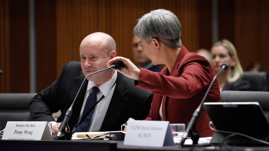Penny Wong covers a microphone while speaking with Greg Moriarty