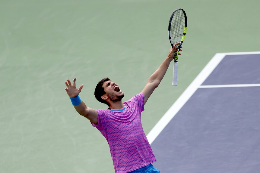 Carlos Alcaraz throws his hands in the air while holding a tennis racquet as he celebrates winning Indian Wells.