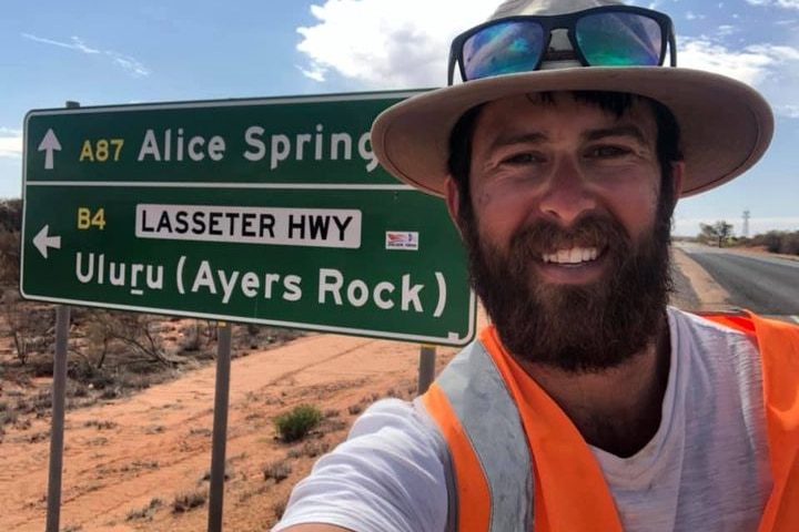 A man stands in front of a road sign for Alice Springs and Uluru. 