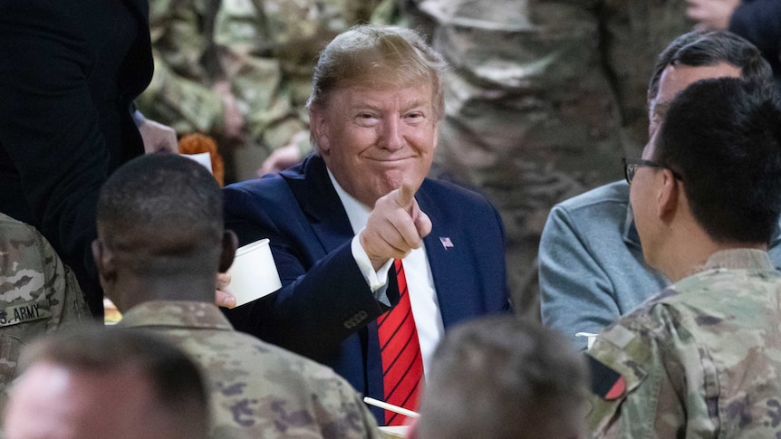President Donald Trump points at the camera while eating during a surprise Thanksgiving Day visit to the troops