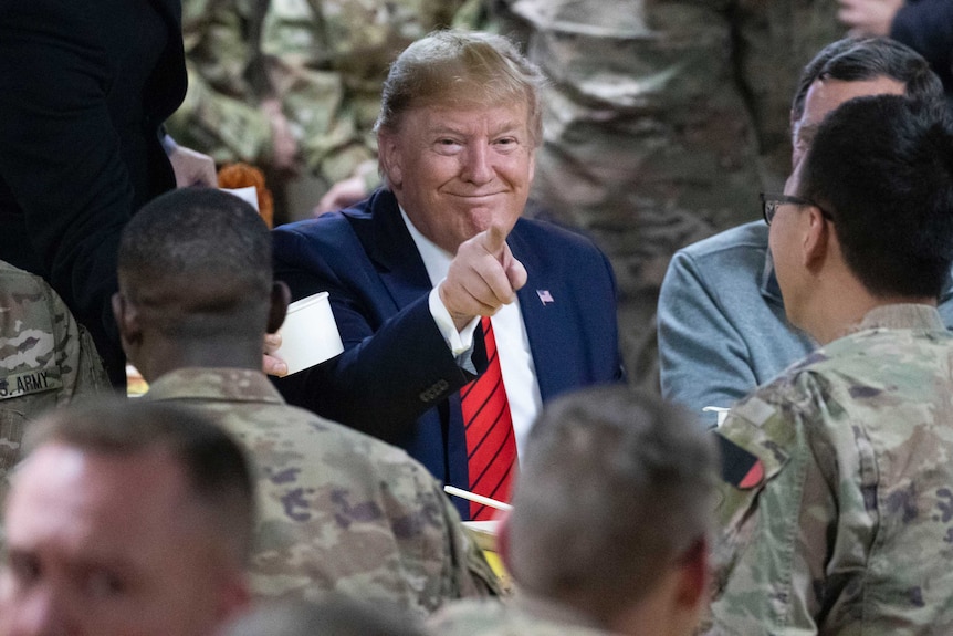 President Donald Trump points at the camera while eating during a surprise Thanksgiving Day visit to the troops