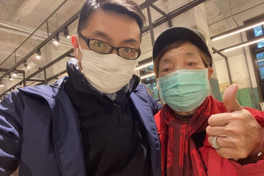 Vincent Hsu and his mother pose for a photo, both are wearing face masks and his mother is giving a thumbs up.