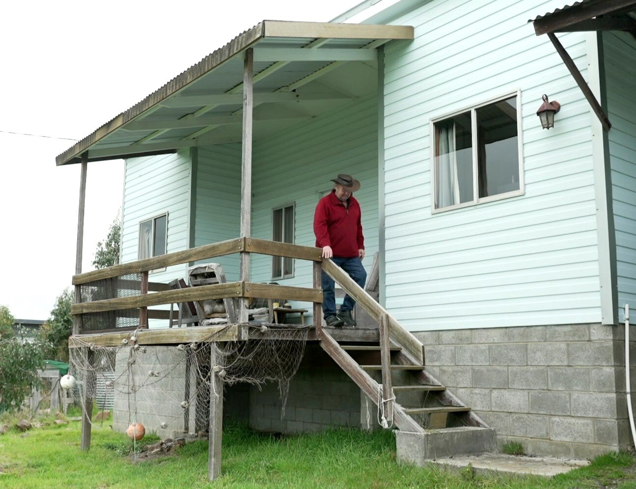 A man in a hat walks down front steps of a house.