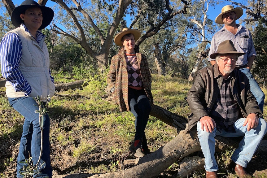 Two women and two men stand by a tree at a rural property. All wear widebrim hats