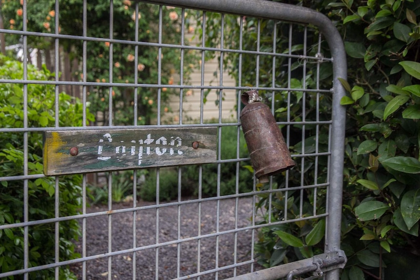 A rusty bell hangs on the gate of a house with the name Layton