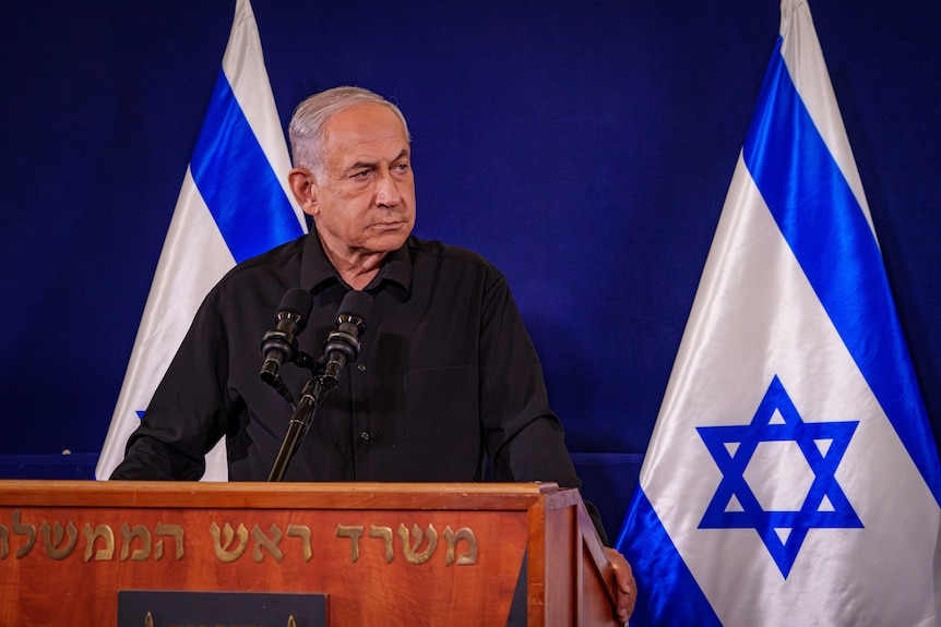 Benjamin Netanyahu in an all-black outfit standing at a lecturn 
