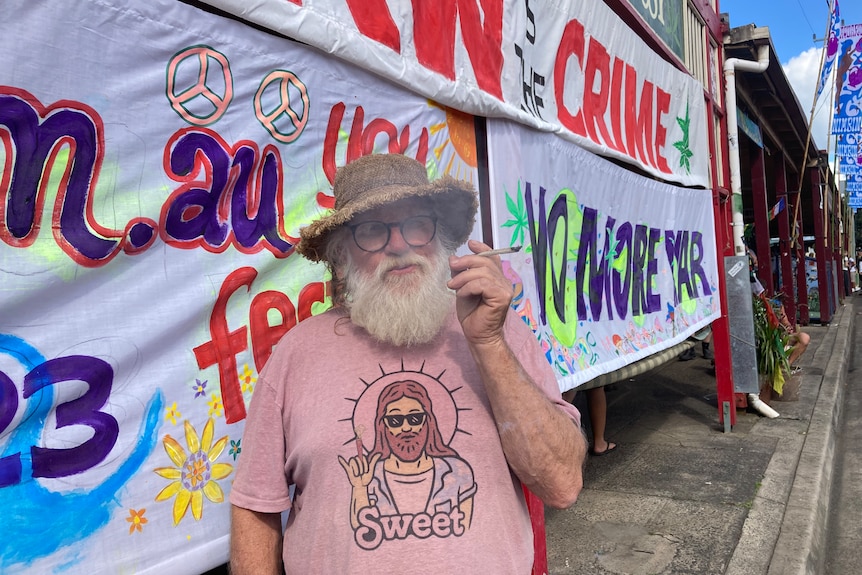 Bearded man in a hat and glasses smoking a joint.