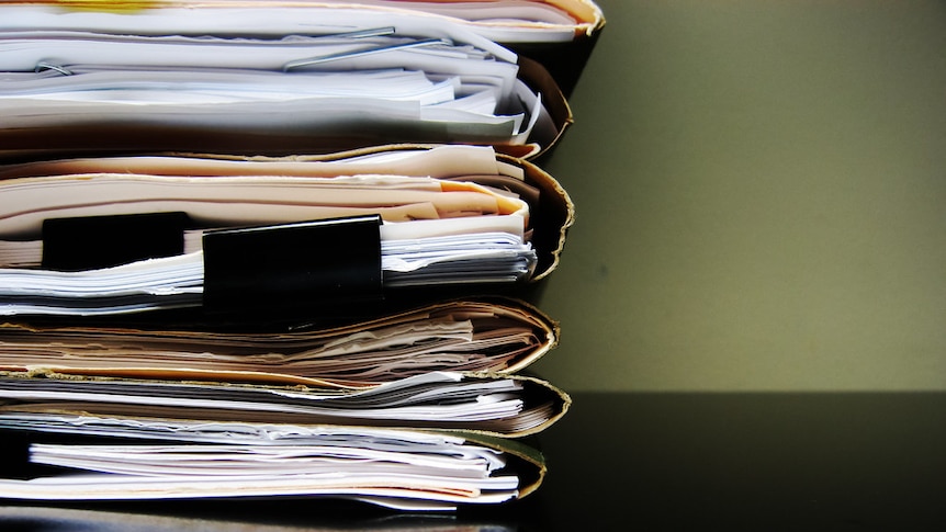 A stack of file and paperwork are seen on a black desk.