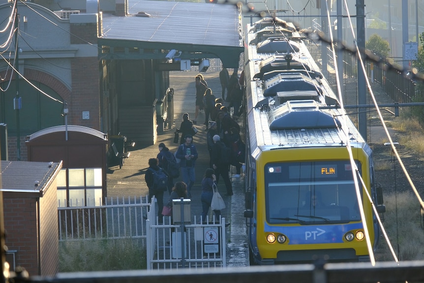 A few dozen commuters board a train at a Melbourne train station.