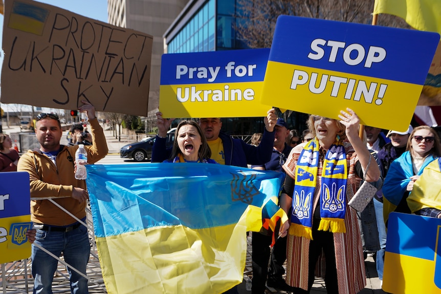 Demonstrators holds signs and Ukrainian flags during a rally.