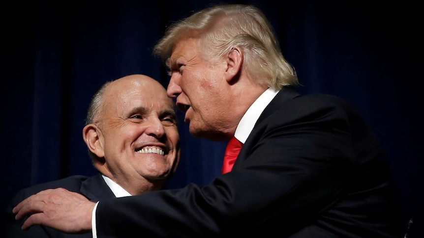 Donald Trump embracing Rudy Giuliani on a dark stage