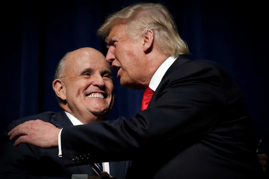 Donald Trump embracing Rudy Giuliani on a dark stage