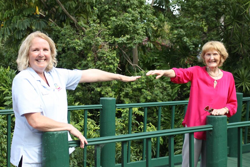 Janice Millington and Margaret Aiston standing on a bridge with arm outstretched towards each other