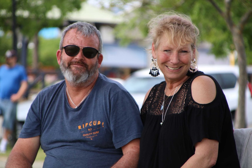 Mid shot of a man and a woman smiling at the camera while sitting outide.