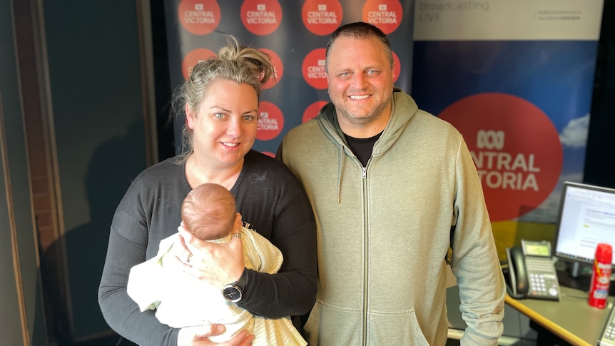 Bec and Leigh Stephens stand in the ABC Bendigo studios holding a baby