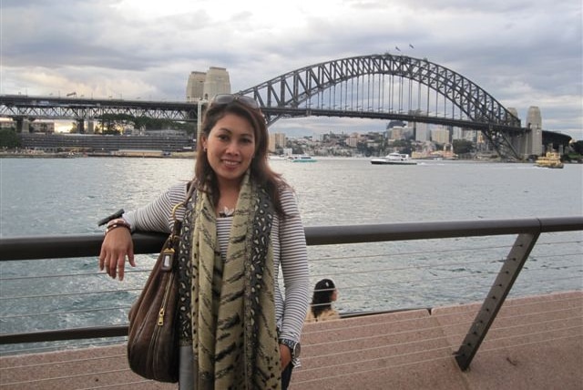 Novy Chardon stands next to a railing with Sydney Harbour Bridge in view, date unknown.