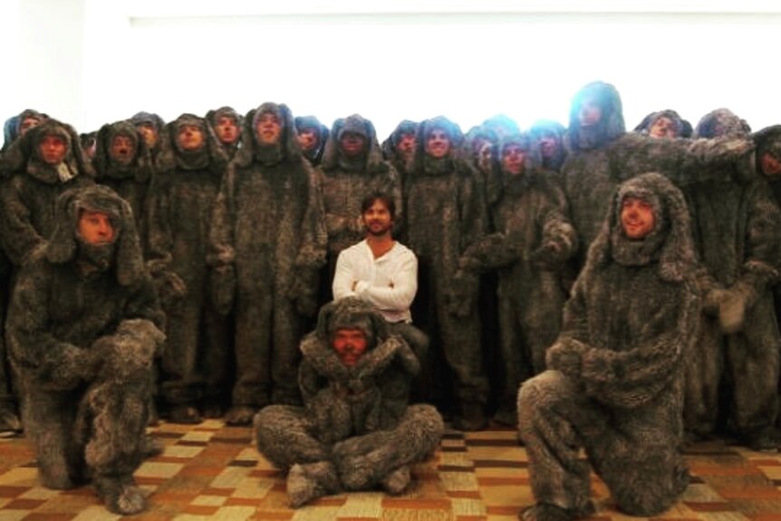 A group of about thirty men all dressed in the same grey dog suit with painted black noses.