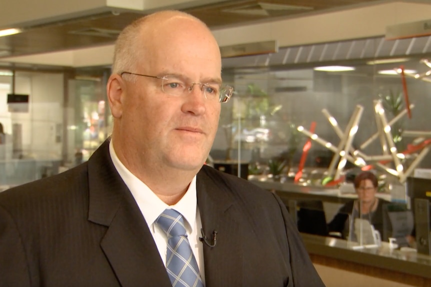 A photo of Mark Lane wearing a suit and talking to the ABC during the interview.