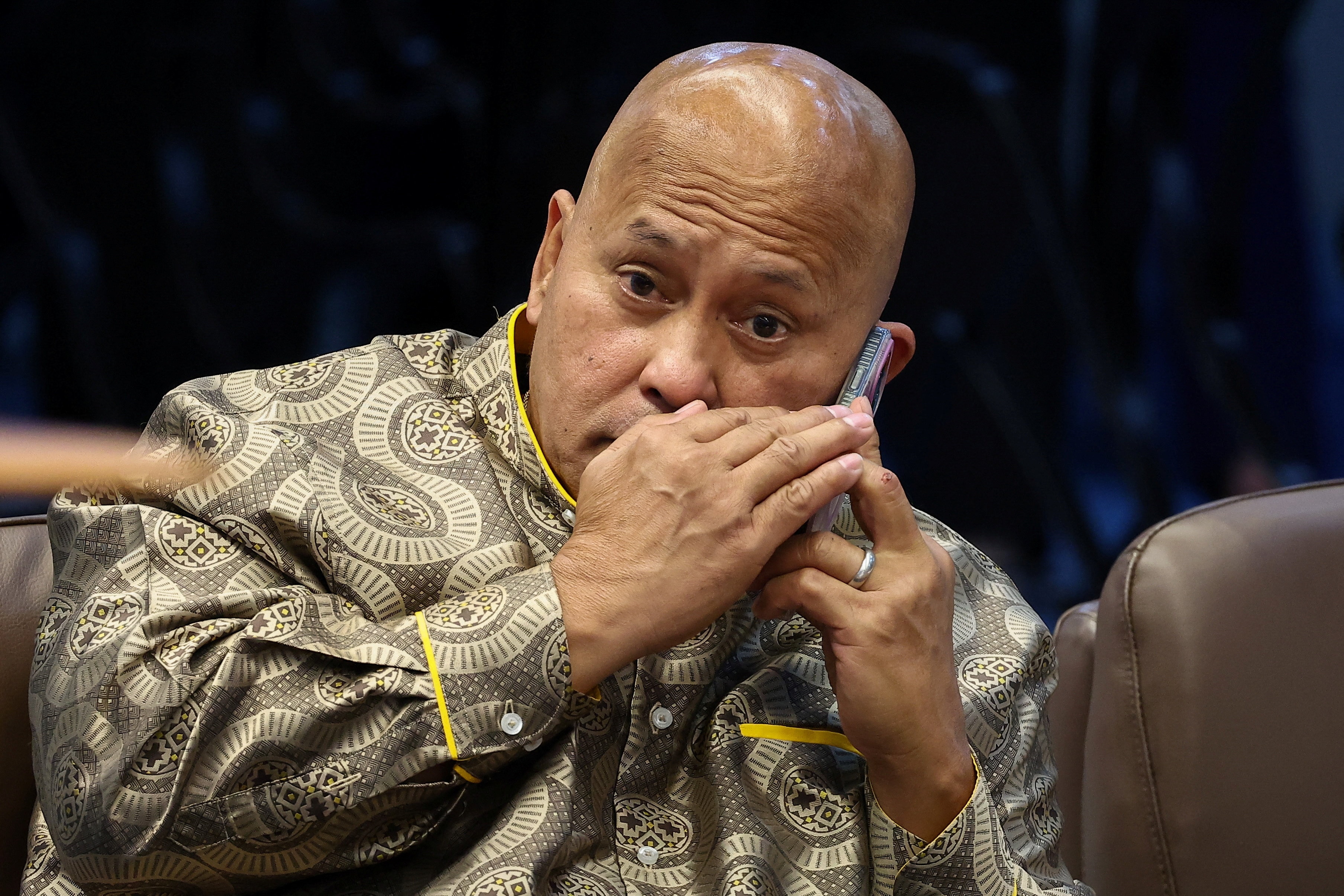 A man holds his hand in front of his mouth as he speaks on the phone.
