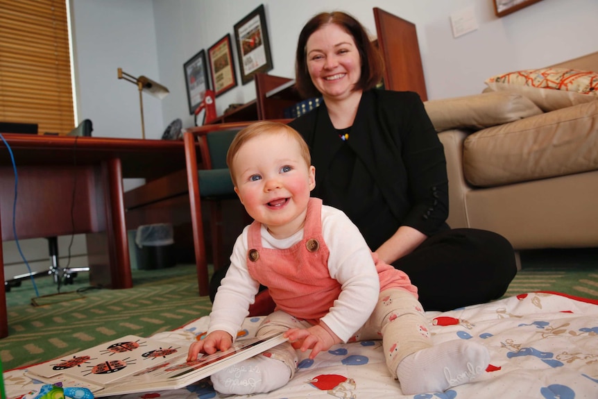 Lisa Chesters smiles wile sitting on the floor with her daughter holding a book