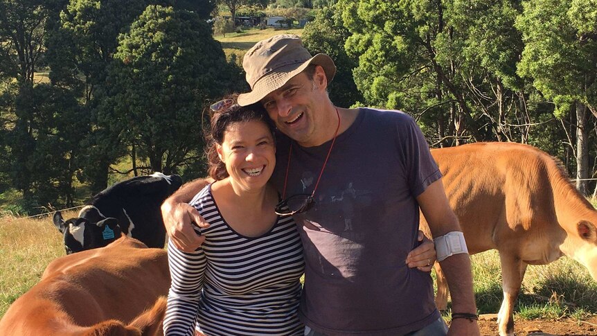 A woman and a man stand with cows on a farm