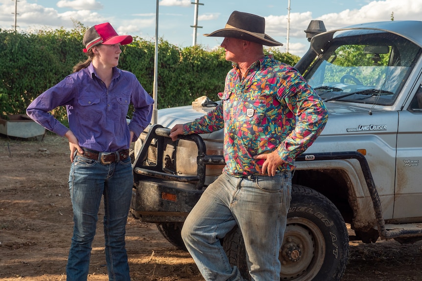 Jacy and her dad Scott stand at the bonnet of a Toyota ute taking after bull riding practice, near Winton, November 2022.