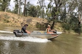 A young man and a woman speeding along a waterway in a tinny.