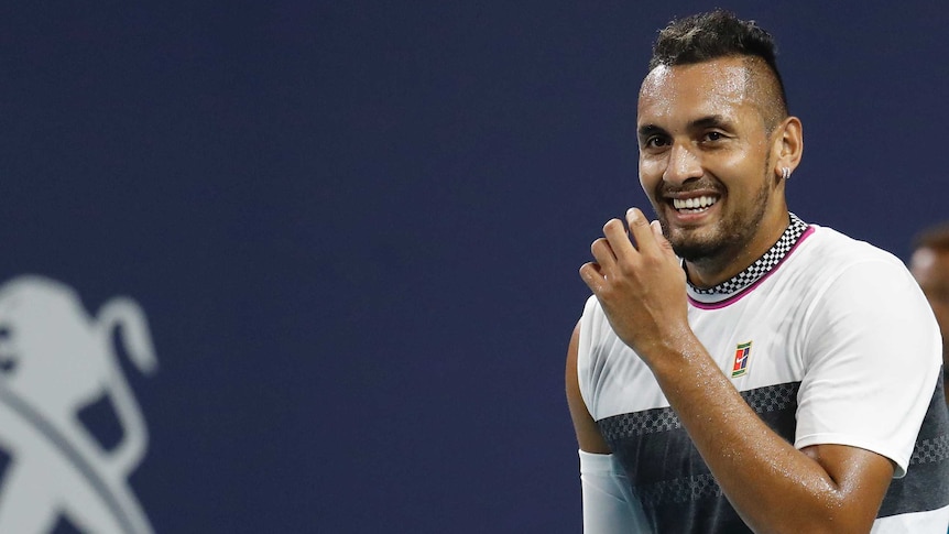 A tennis player smiles behind his raised hand on court during a match.