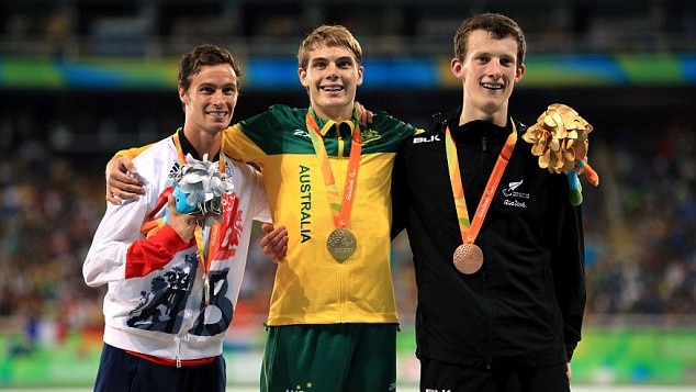 Three men stand smiling on a podium, James Turner wearing green and gold in the middle
