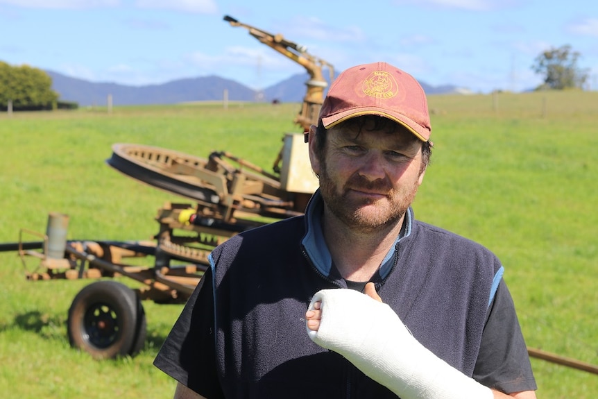 Dairy farmer Damien Carpenter holds up his injured hand in front of the irrigator that maimed him.
