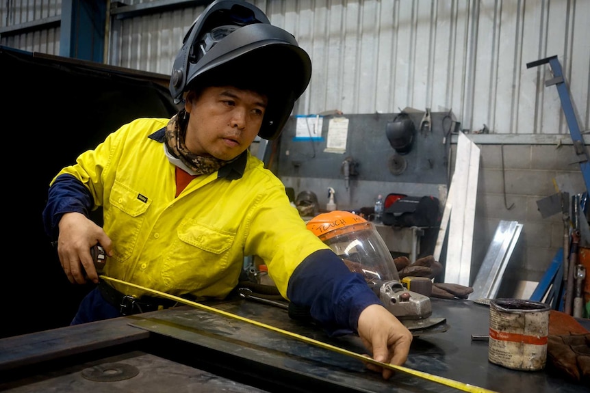 A man with a welding helmet works in a shed.