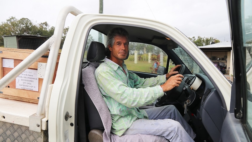 A man inside a car with his hands on the steering wheel and the door open