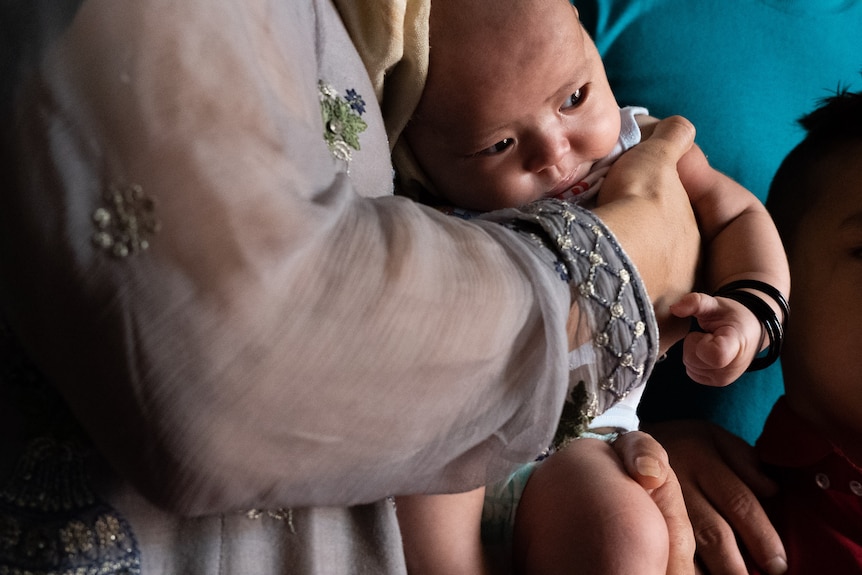 A small child with black bangles is held against her mother's abdomen. 