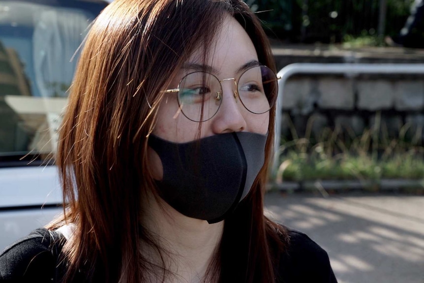 A close photo of Caitlyn who is wearing a black shirt, face mask and glasses.