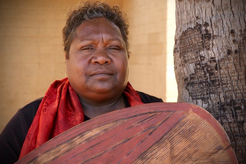 A dark-skinned woman wearing a red scarf looks directly into the camera