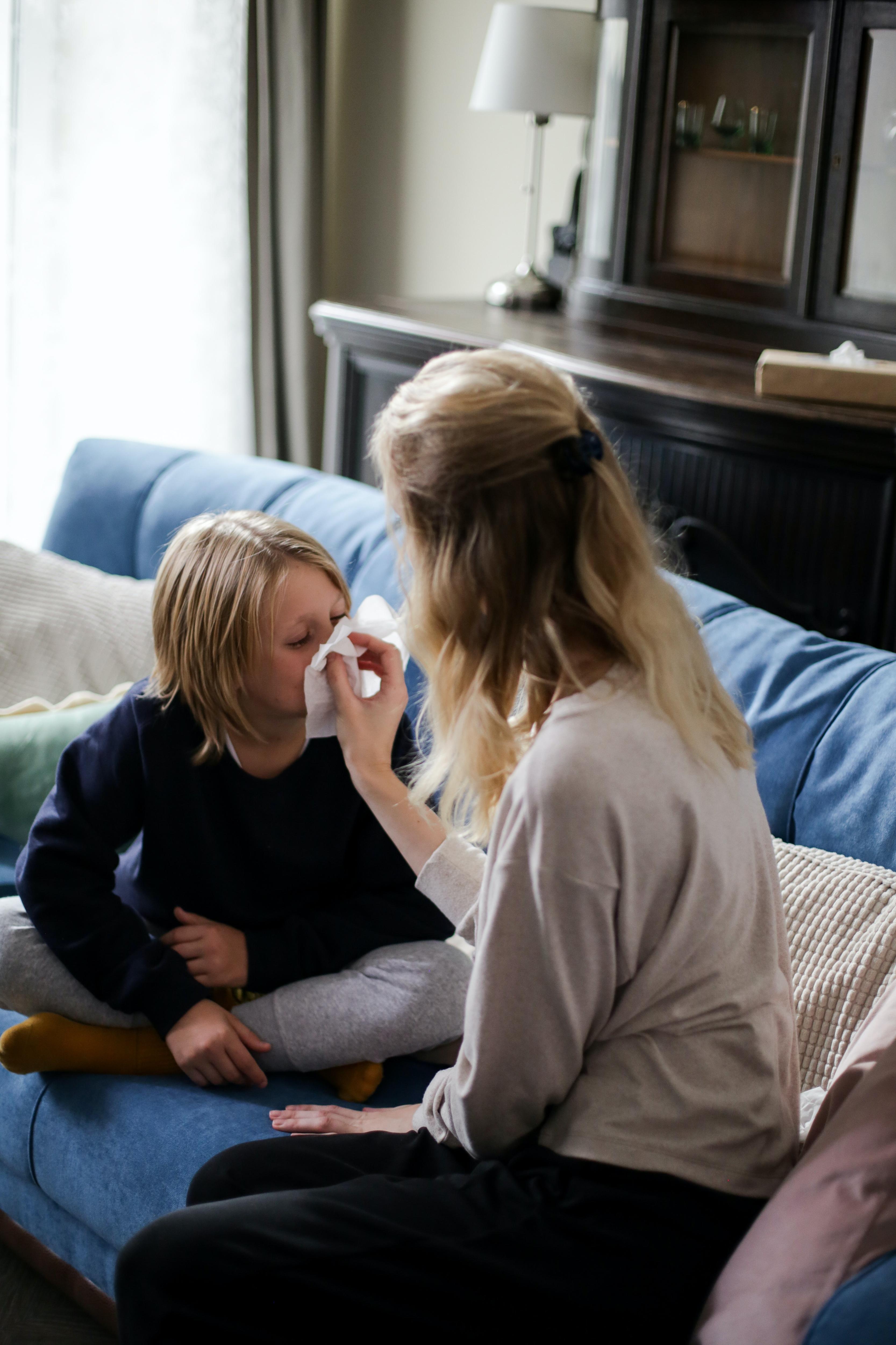 A woman blows a young child&#x27;s nose.