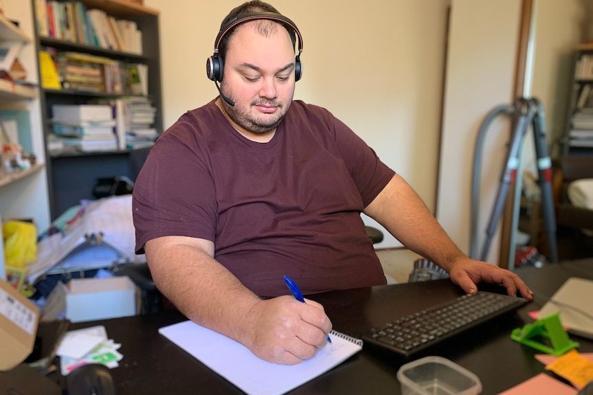 A man sits at a computer wearing a telephone headset.