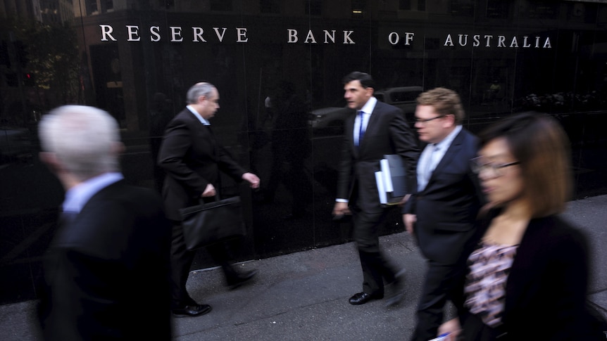 Four men and one woman, all wearing suits, walk in front of the Reserve Bank of Australia building in Sydney.