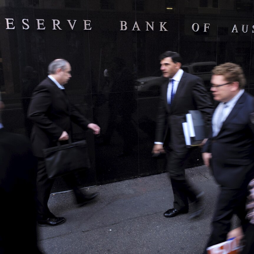 People in office clothes walk in front of the Reserve Bank of Australia building. 