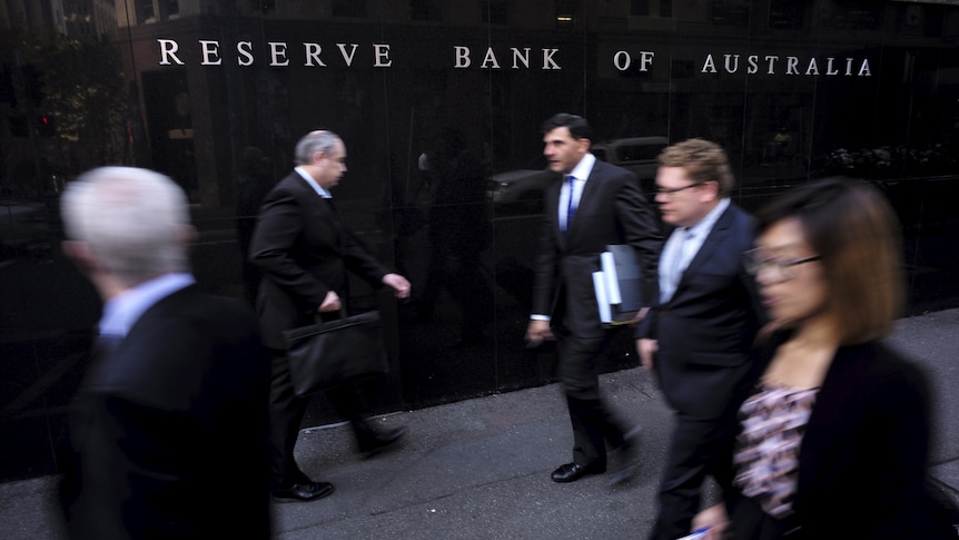 People in office clothes walk in front of the Reserve Bank of Australia building. 