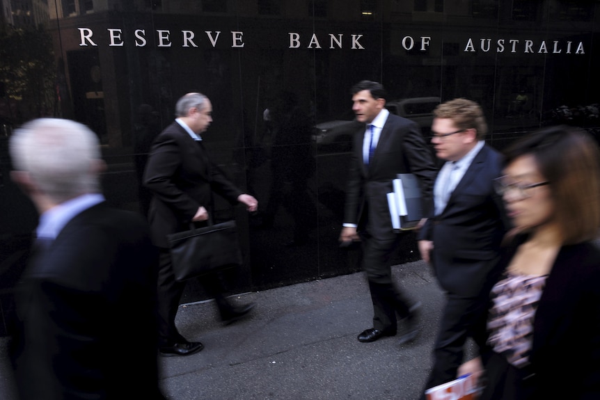Four men and one woman, all wearing suits, walk in front of the Reserve Bank of Australia building in Sydney.
