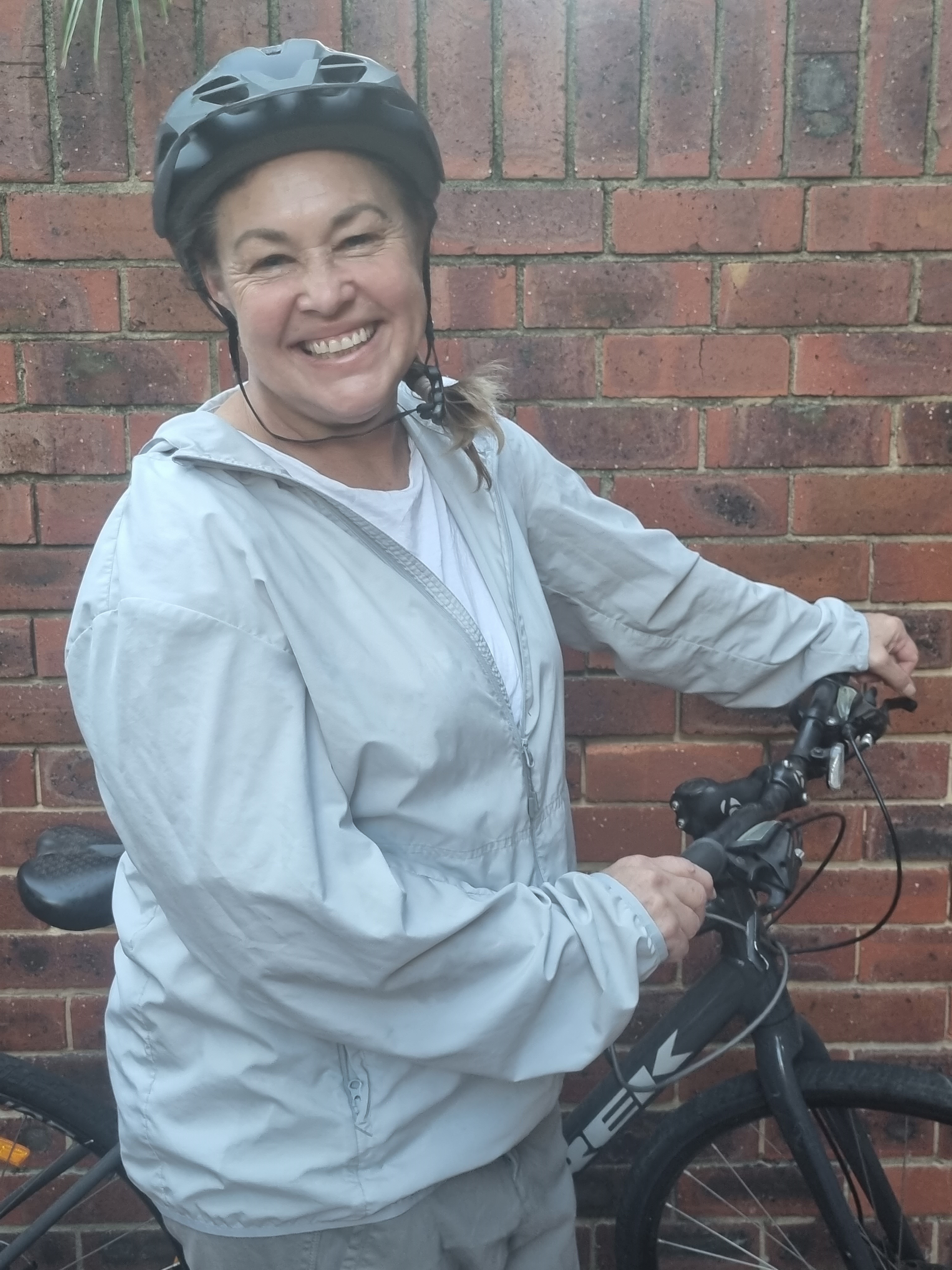 A woman in a bike helmet, holding her bike, grins at the camera.