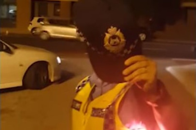 A police officer stands holding her hat out in front of her face to prevent it being caught on camera.