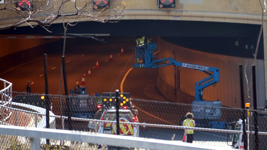 Two workers in a cherry picker working on the ceiling of a traffic tunnel.