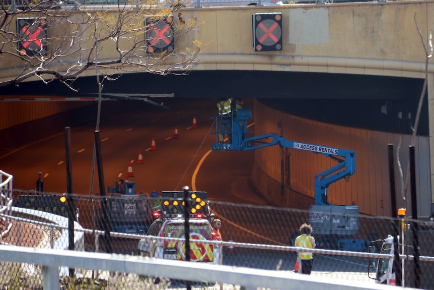 Two workers in a cherry picker working on the ceiling of a traffic tunnel.