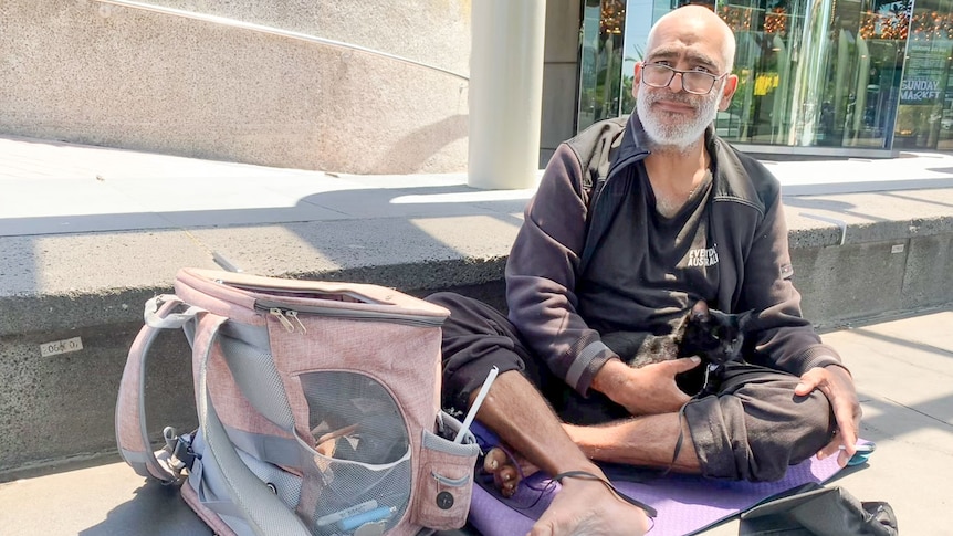 Homeless man Morgan sitting on a yoga mat with his cat around the Arts centre building near Melbourne CBD.