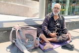 Homeless man Morgan sitting on a yoga mat with his cat around the Arts centre building near Melbourne CBD.